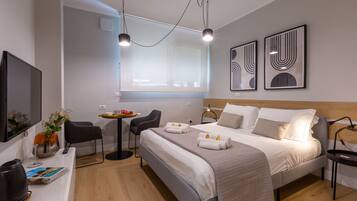 Una habitación de hotel moderna con una cama grande, un escritorio con una silla, una mesita con otra silla y obras de arte en las paredes.