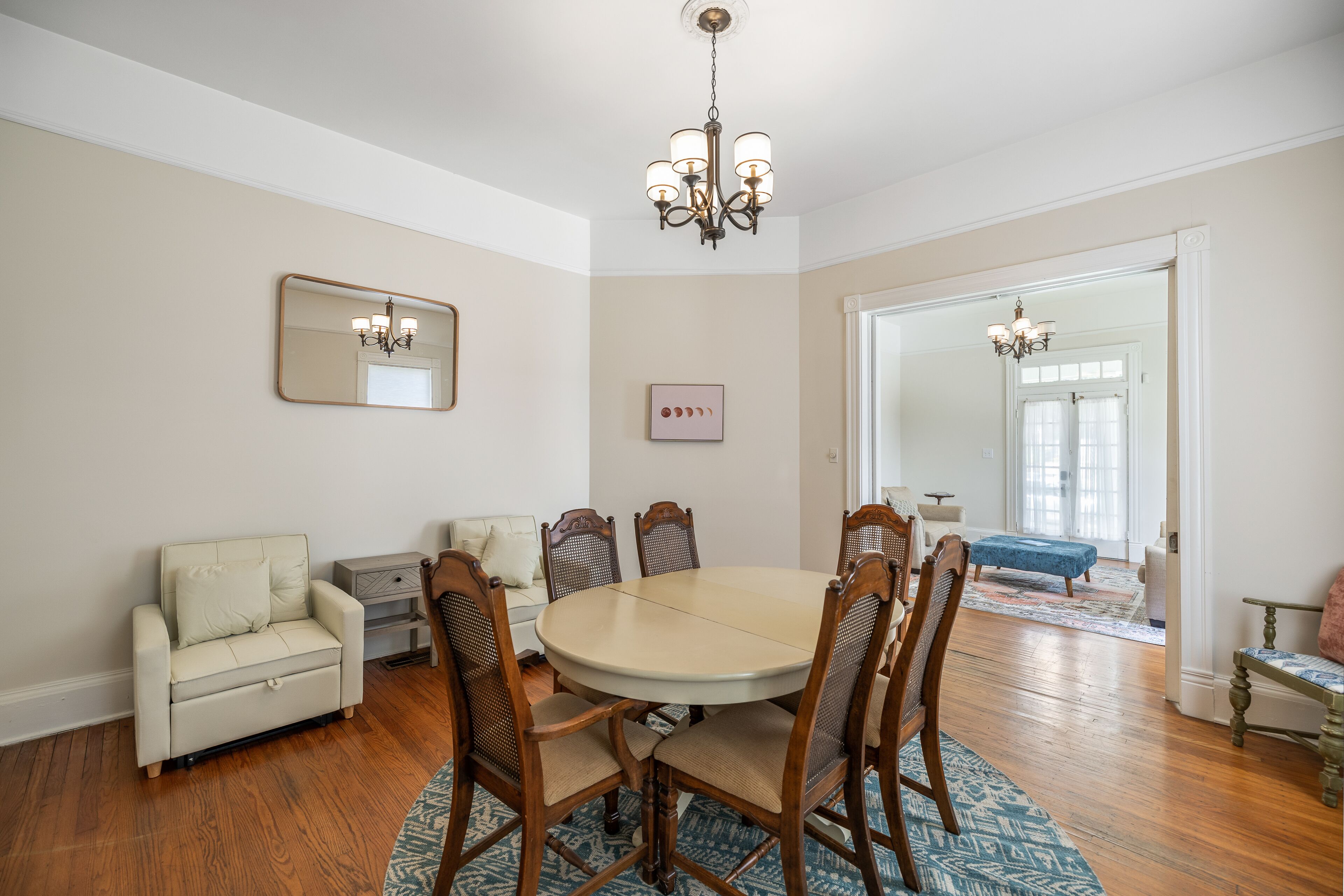 A dining room with a round table, six chairs, a sofa, and a chandelier.