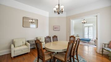 A dining room with a round table, six chairs, a sofa, and a chandelier.