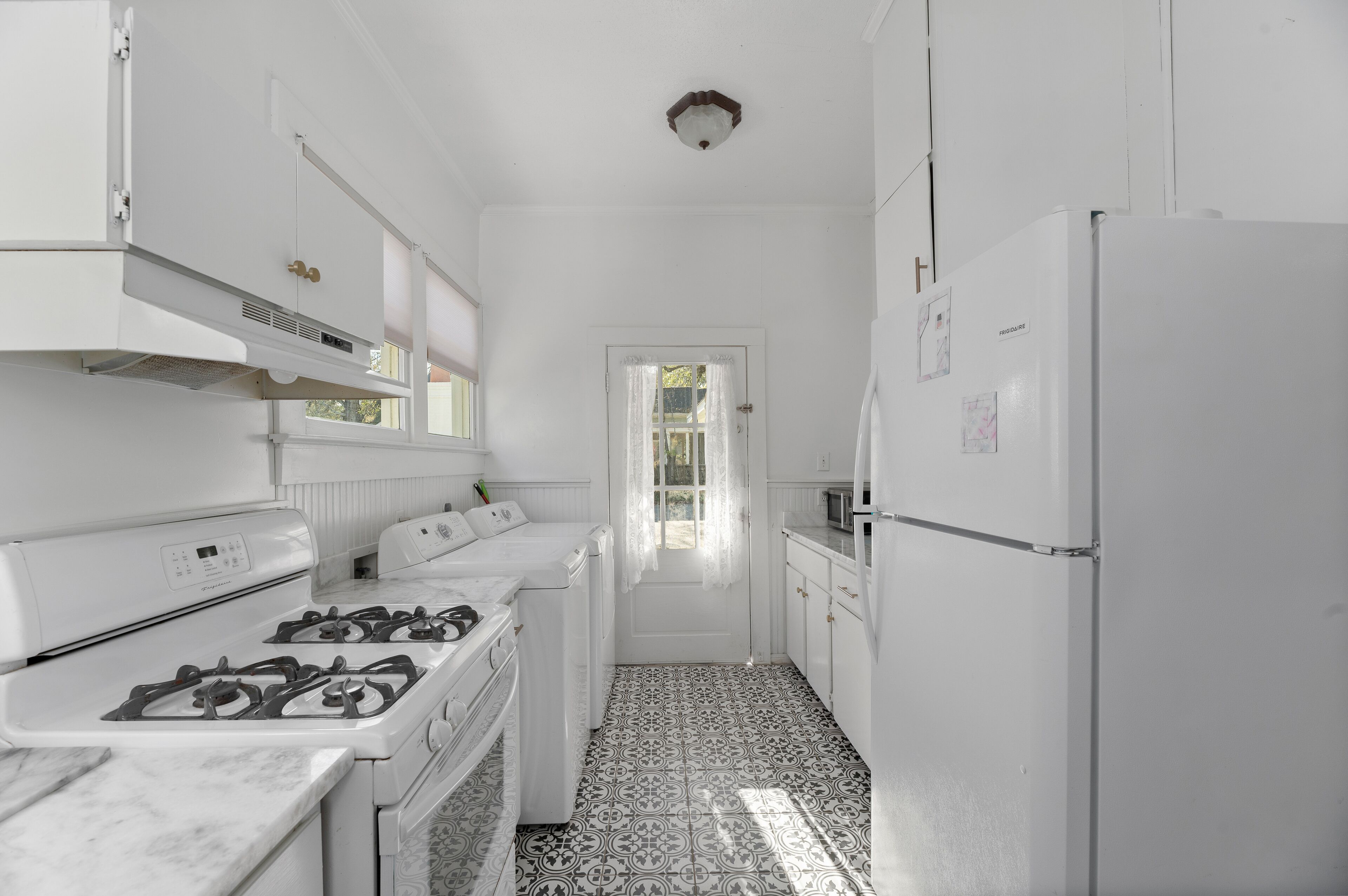 Une cuisine étroite avec des meubles blancs, une cuisinière et un réfrigérateur.