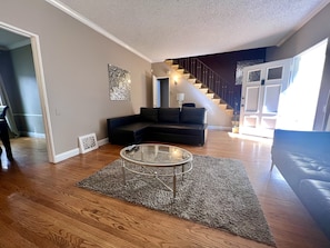 Una sala de estar con un sofá modular, una mesa de centro de vidrio y una escalera que conduce a un nivel superior.
