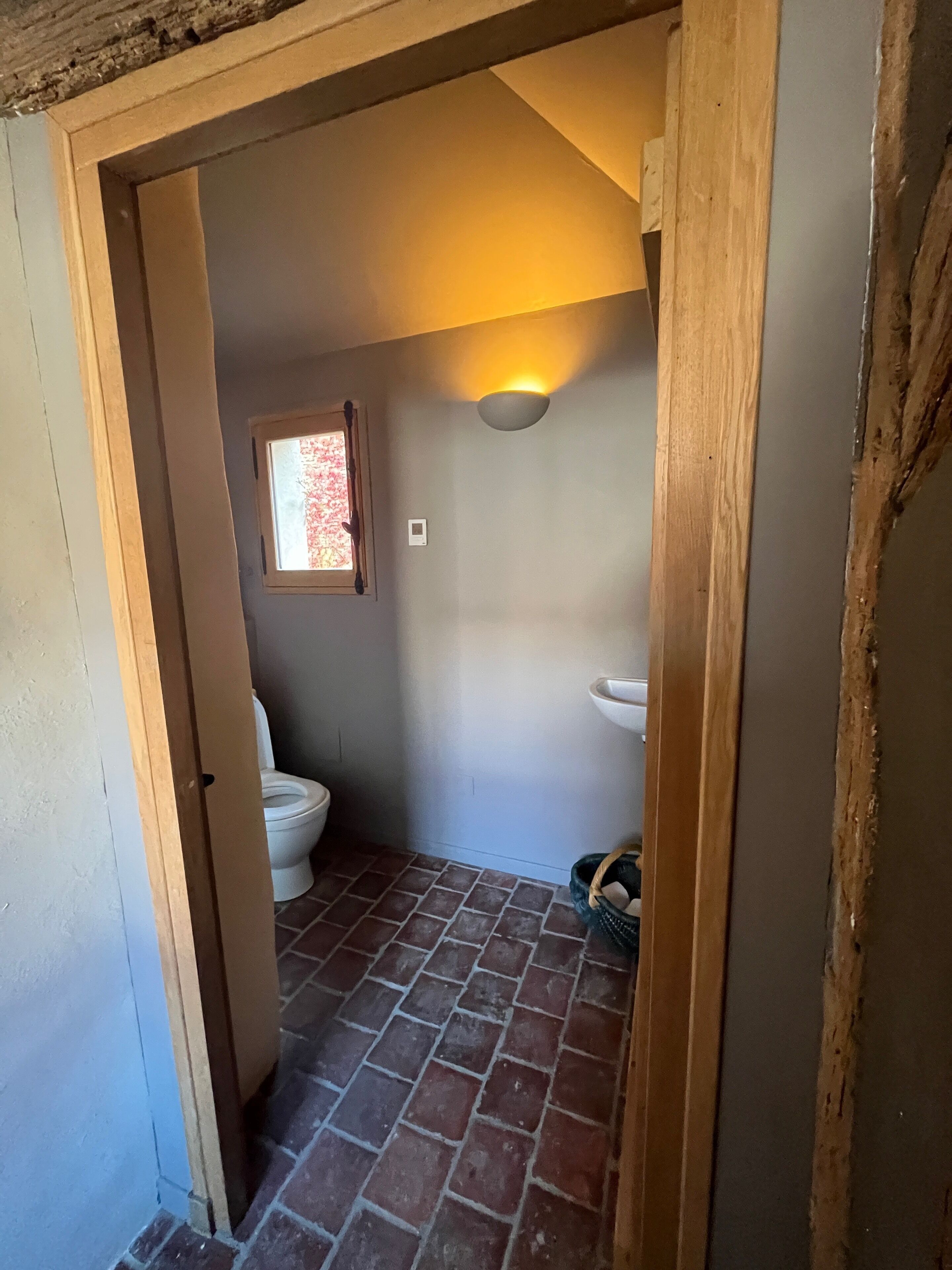 A bathroom with a toilet, a window, a sink, and a wall-mounted light fixture.