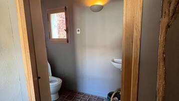A bathroom with a toilet, a window, a sink, and a wall-mounted light fixture.