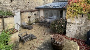 Un edificio de piedra con techo de tejas, un pequeño jardín con un banco y una planta en maceta.