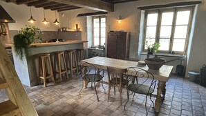 Una cocina rústica con una mesa de madera, taburetes de bar, lámparas colgantes y suelo de ladrillo.