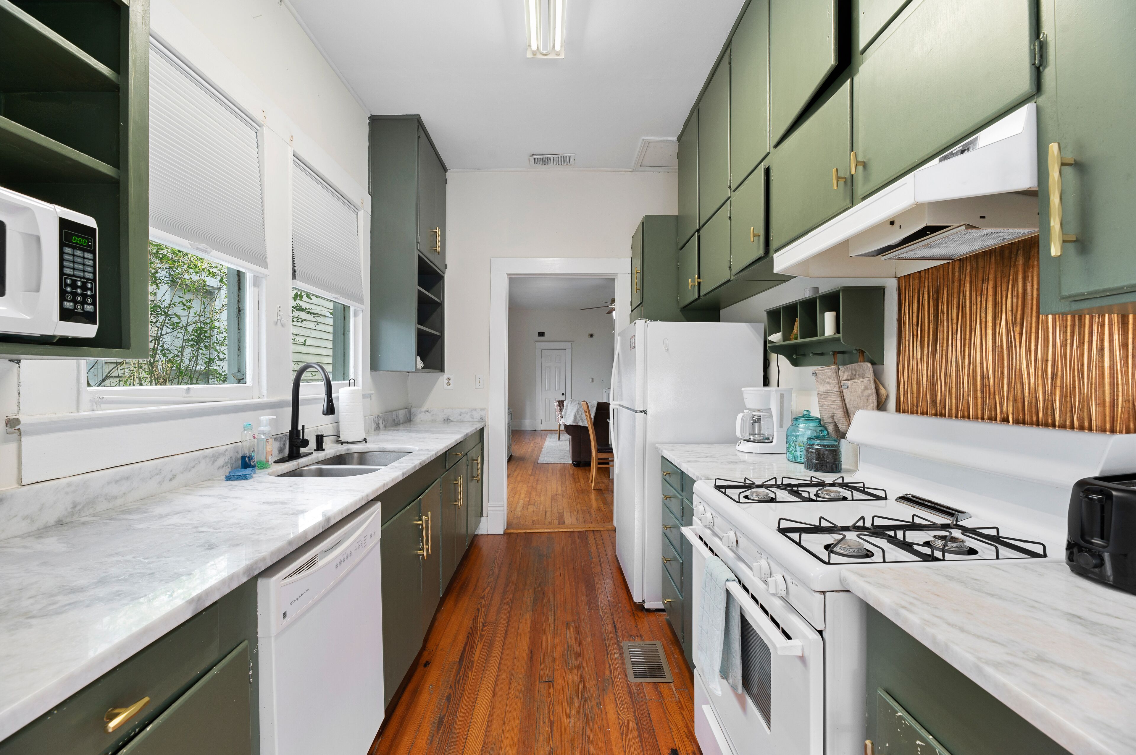 A kitchen with green cabinets, white appliances, and a wooden floor.