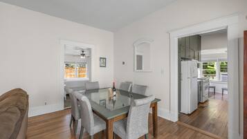 A dining area with a glass-top table, six grey upholstered chairs, and a brown couch.