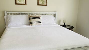 A neatly made bed with white linens, a striped pillow, and two framed botanical prints on the wall.