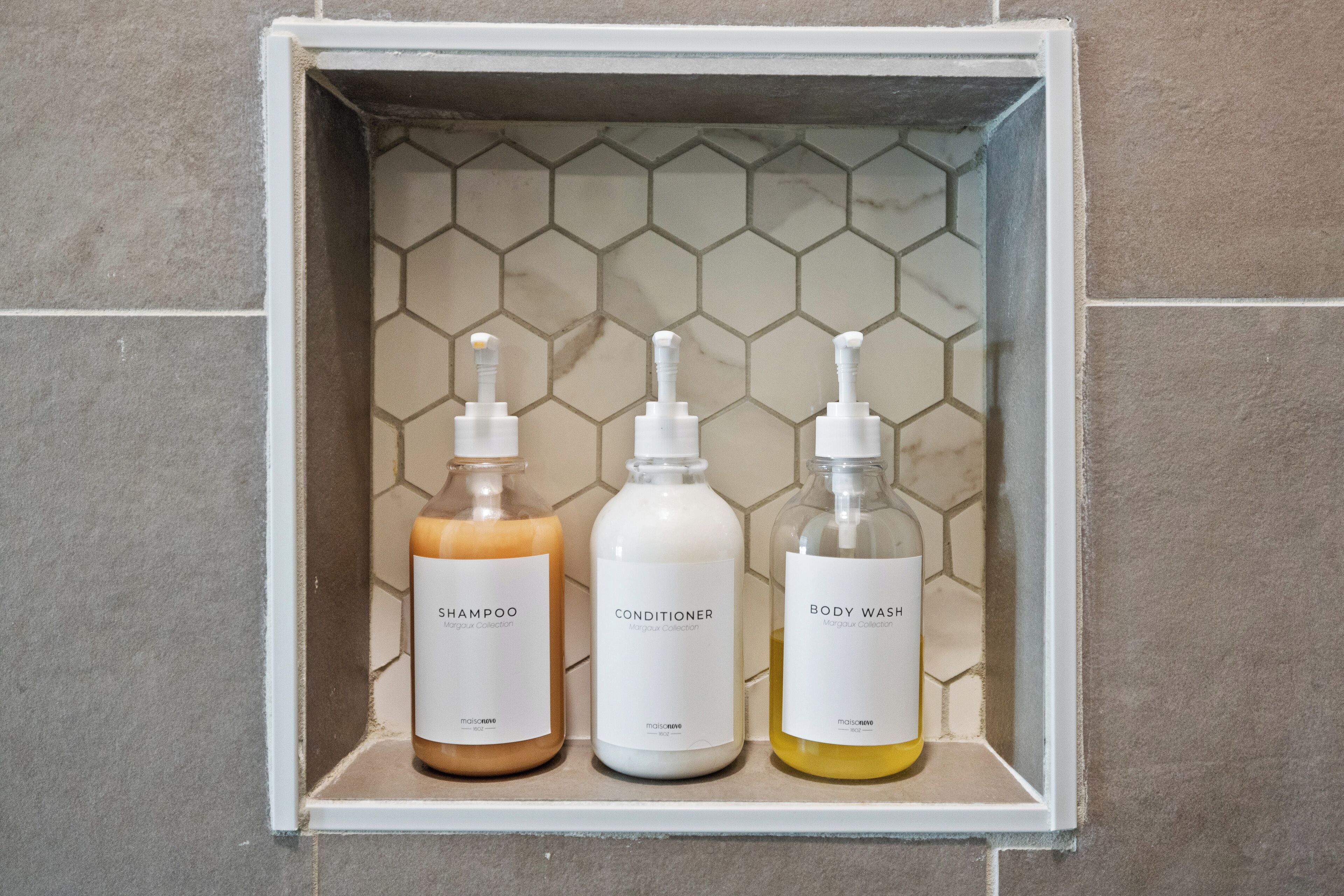 A bathroom shelf with three bottles of shampoo, conditioner, and body wash.