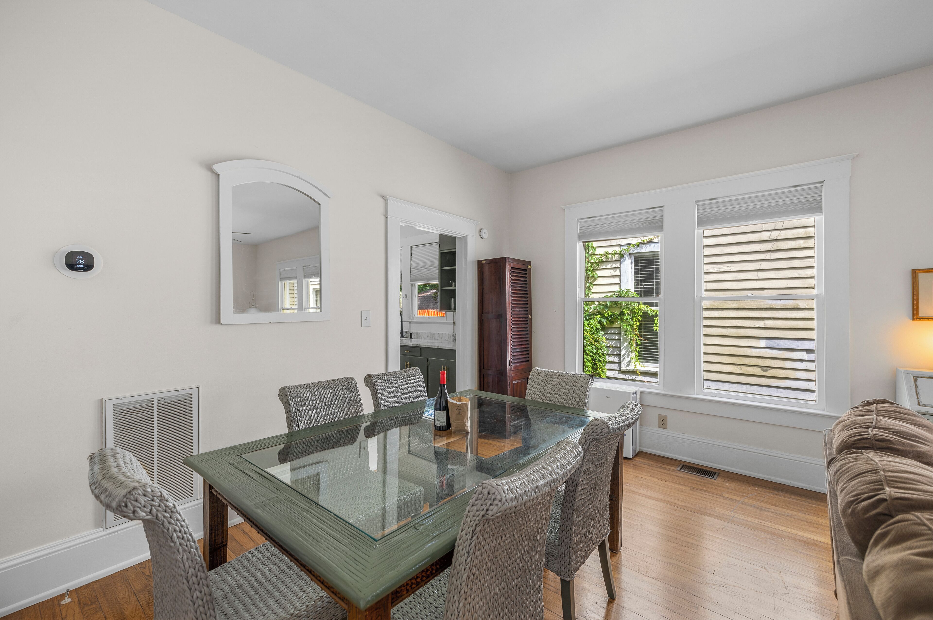 A dining area with a glass-top table, wicker chairs, and a view of the outdoors through large windows.