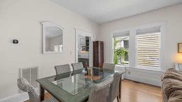 A dining area with a glass-top table, wicker chairs, and a view of the outdoors through large windows.