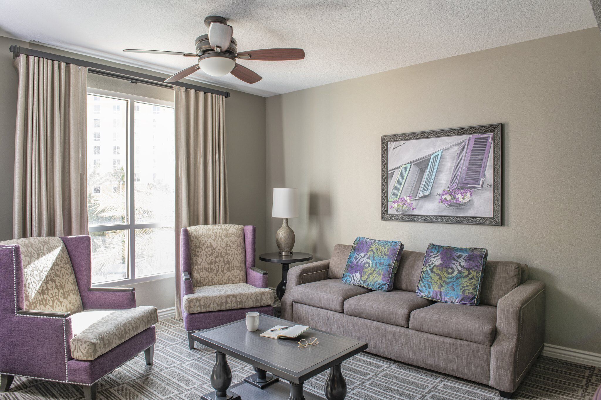 A hotel room with a sofa, two armchairs, a coffee table, a lamp, and a ceiling fan.