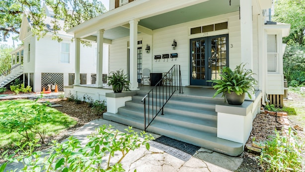 A two-story house with a covered porch, a front door, and a staircase leading to the entrance.