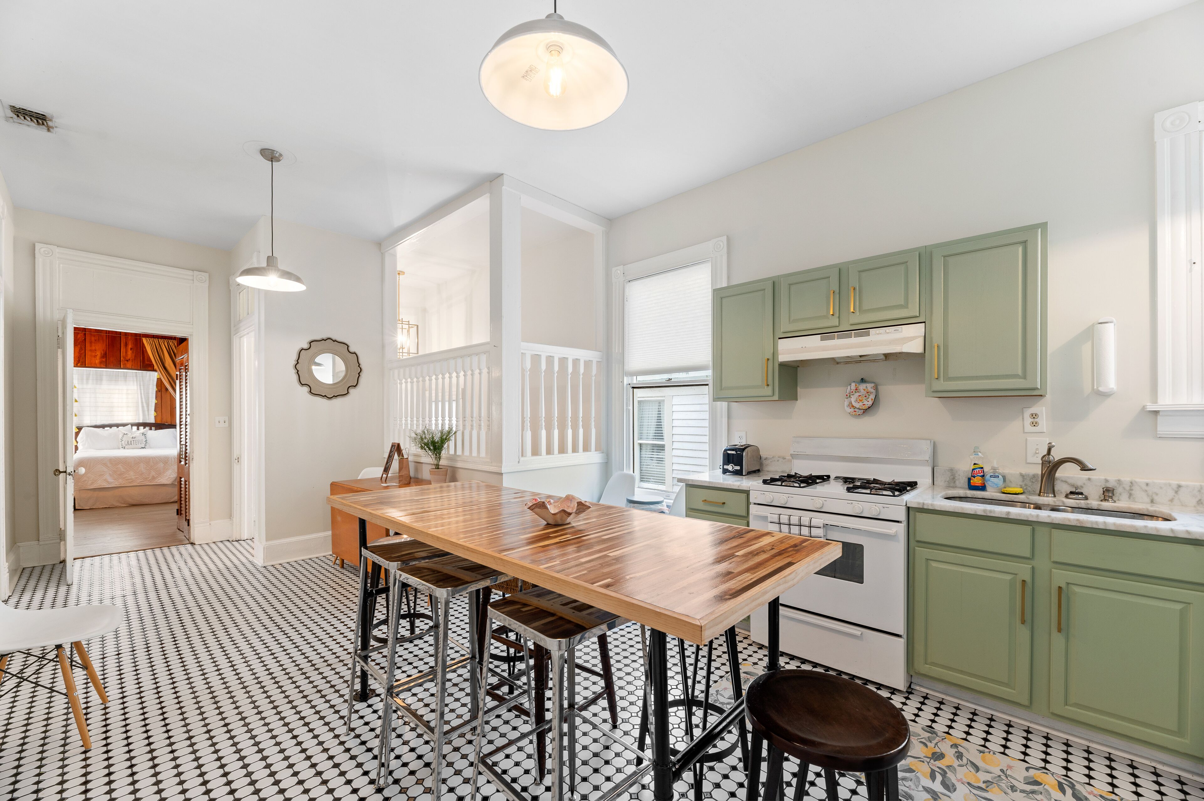 A kitchen with a wooden table and stools, green cabinets, and a white countertop.