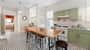 A kitchen with a wooden table and stools, green cabinets, and a white countertop.