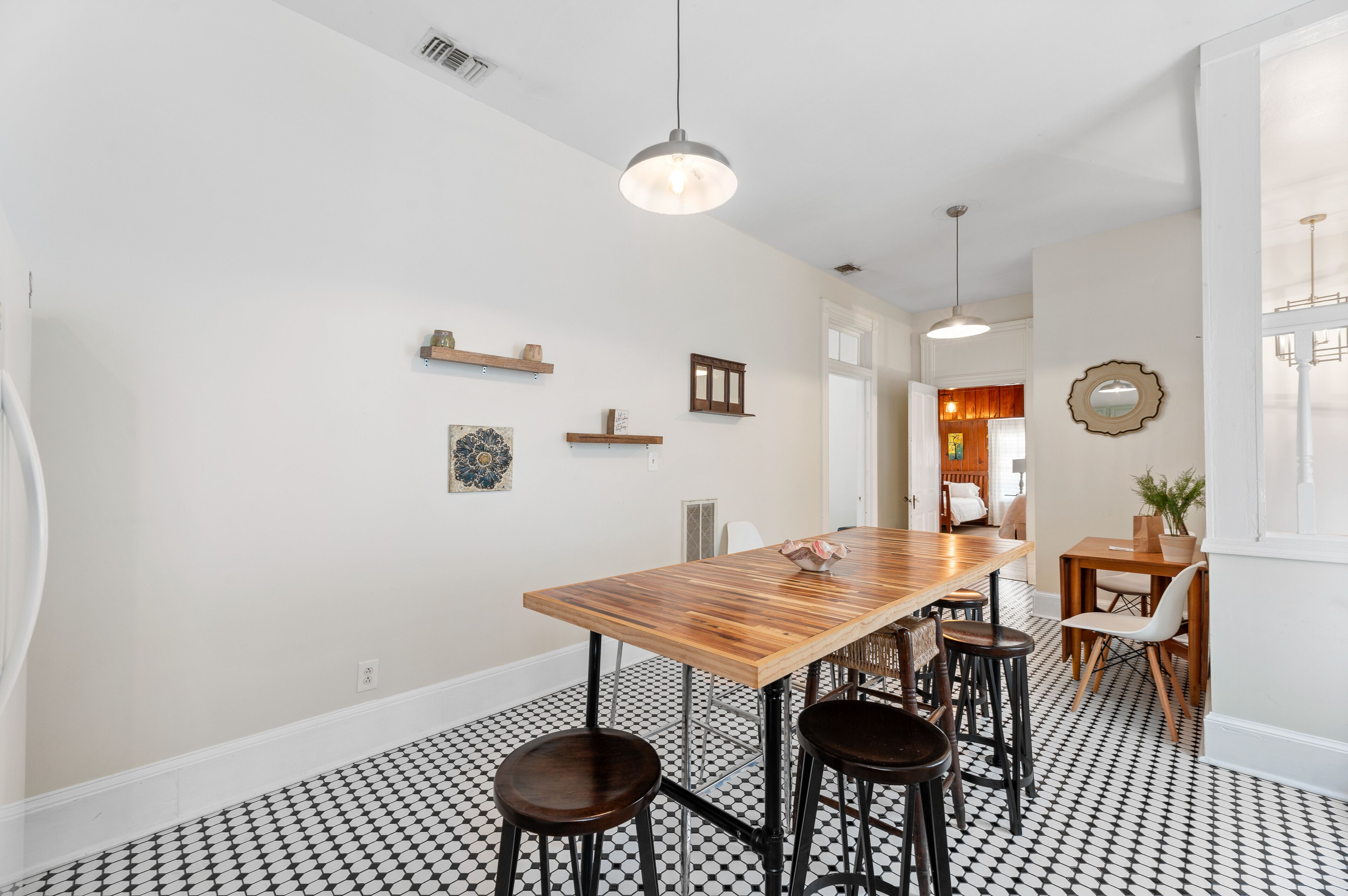 A dining area with a wooden table, black and white patterned floor, and pendant lighting.