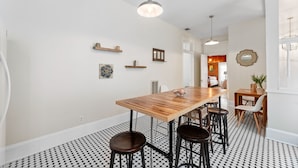 A dining area with a wooden table, black and white patterned floor, and pendant lighting.
