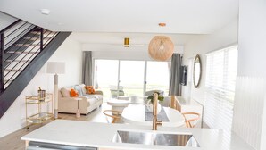Uma cozinha moderna com uma ilha central, uma área de jantar com mesa redonda e uma escada à esquerda.