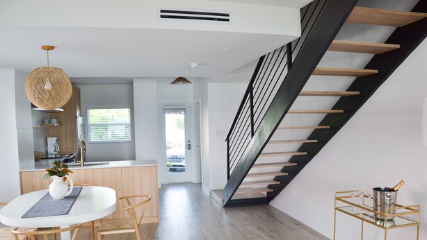 A modern kitchen with a dining area, a staircase, and a cart with glasses and a bottle.