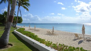 Uma praia com cadeiras de praia e guarda-sóis, palmeiras e uma vista clara do oceano.