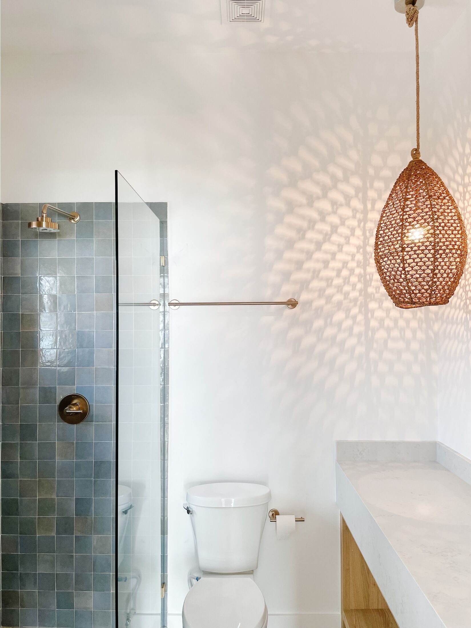 Un baño con cabina de ducha de vidrio, inodoro blanco y lámpara colgante.