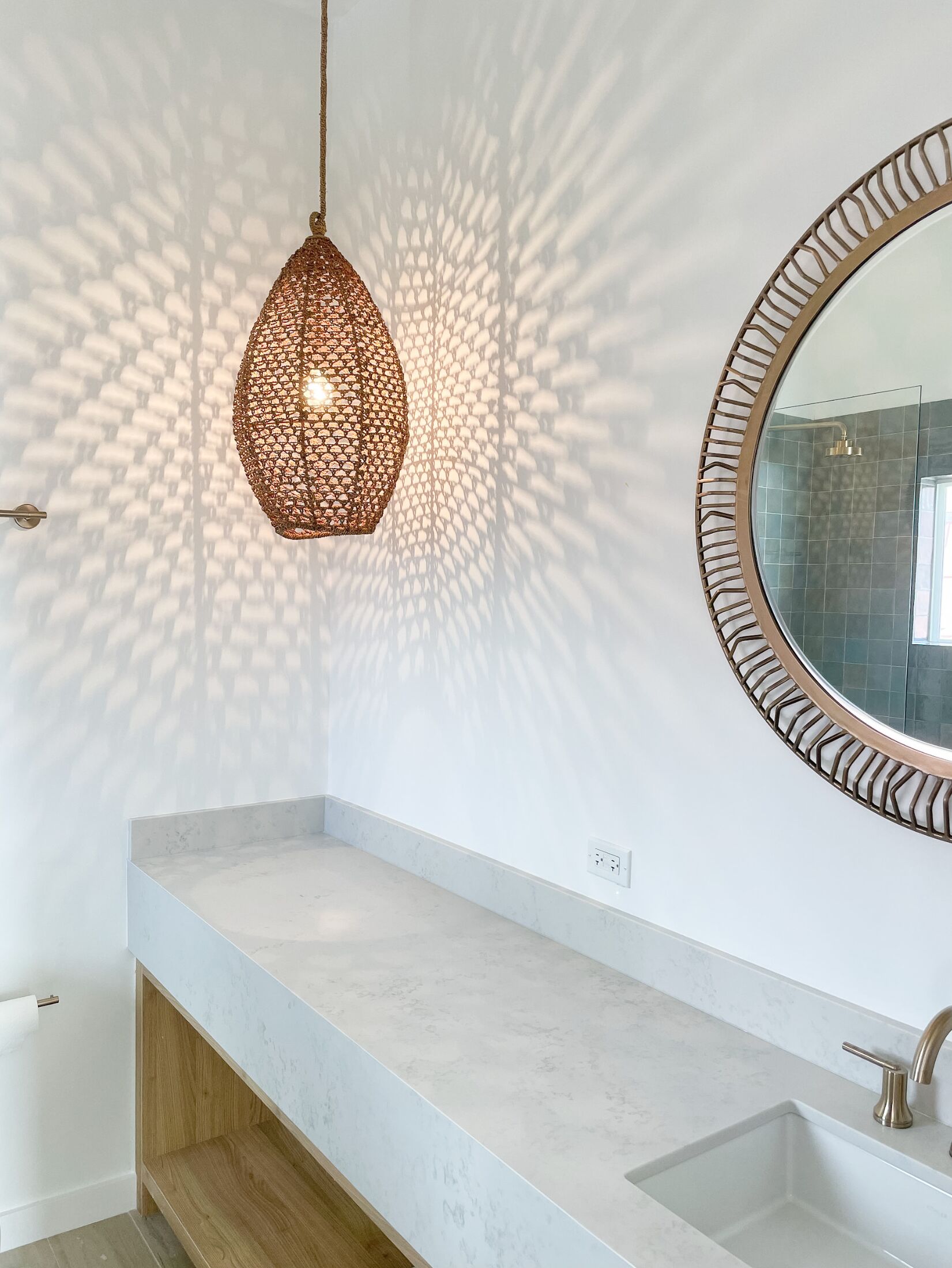 Une salle de bain dotée d’un comptoir en marbre, d’un miroir rond orné d’un cadre décoratif et d’un luminaire suspendu.