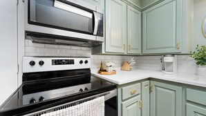 Una cocina con microondas, horno y estufa de acero inoxidable, armarios verde claro y encimera blanca.