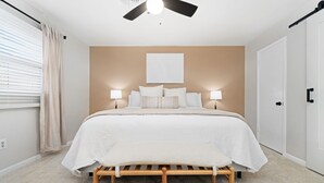 Un dormitorio con cama, lámparas de noche, ventilador de techo y una puerta.
