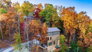 Ein modernes, zweistöckiges Haus, umgeben von einem dichten Wald mit Herbstlaub.