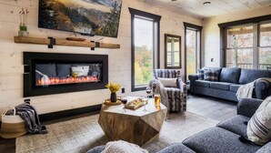 Ein gemütliches Wohnzimmer mit Kamin, einem großen an der Wand befestigten Fernseher und einer komfortablen Sitzecke mit Sofa und Couchtisch.