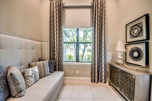 A living room with a sofa, patterned cushions, a window with curtains, a lamp, and wall art.