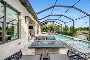 A covered outdoor swimming pool with lounge chairs and a table, surrounded by a glass enclosure.