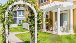 A pathway leading to a white pergola with chairs, surrounded by a white picket fence and lush greenery. - Villas at Seven Dwarfs (Kissimmee)