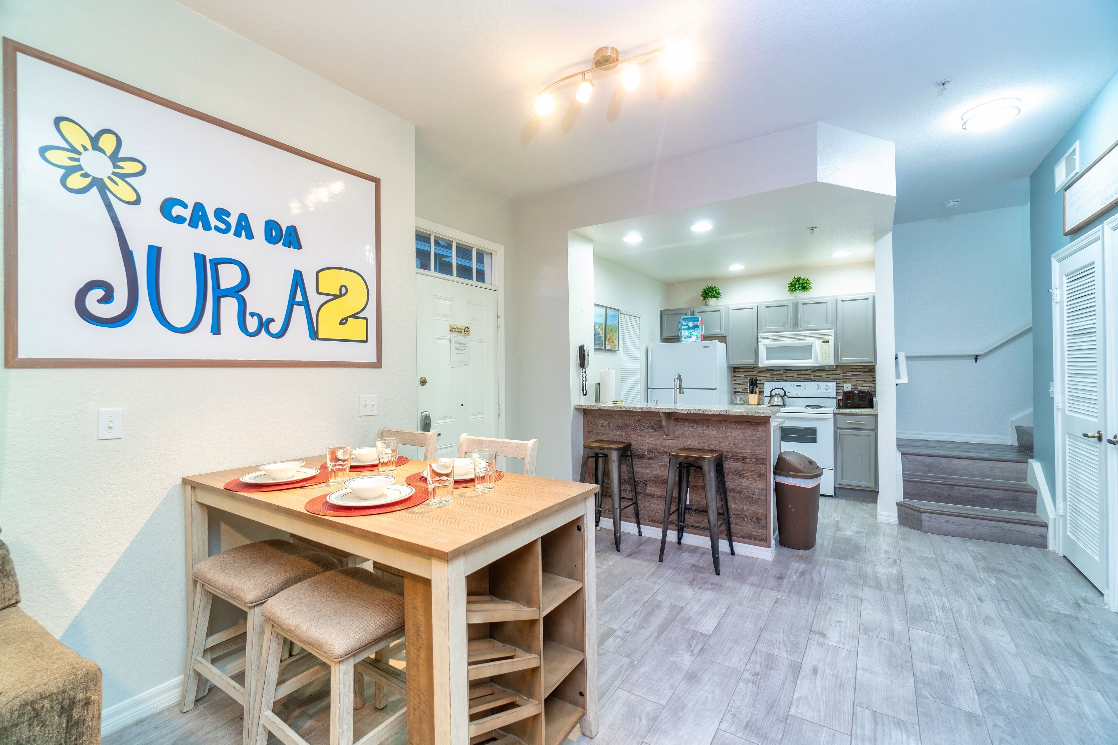 A modern kitchen with white cabinets, a microwave, and a sink. There is a dining area with a wooden table and chairs.