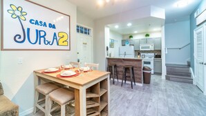 A modern kitchen with white cabinets, a microwave, and a sink. There is a dining area with a wooden table and chairs. - Villas at Seven Dwarfs (Kissimmee)