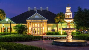 A hotel with a well-lit entrance, a fountain, and manicured landscaping. - Villas at Seven Dwarfs (Kissimmee)