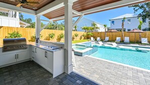 A covered outdoor kitchen with a grill, adjacent to a swimming pool with lounge chairs.