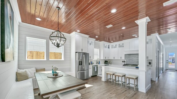 A modern kitchen with wooden ceiling, white cabinetry, and a central island with stools.