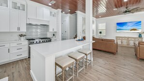 A modern kitchen with white cabinetry, a large island with stools, and a ceiling fan.