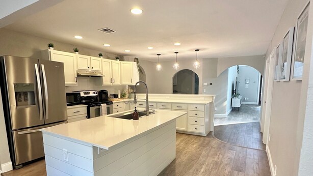 A modern kitchen with a large island, stainless steel appliances, and light wood flooring.