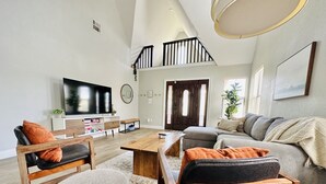 A spacious living room with a large TV, a wooden coffee table, and a grey sofa.