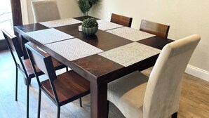A dining room with a rectangular table, six chairs, a potted plant, and a painting on the wall.