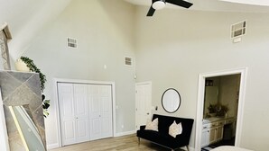 A bedroom with a bed, a black sofa, a ceiling fan, and a white door.