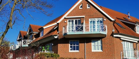 A two-story brick house with a balcony, a chimney, and a clear blue sky.