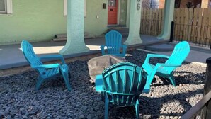 Une terrasse avec quatre chaises Adirondack bleues, un petit foyer extérieur et une maison à l’extérieur vert et à la porte rouge.