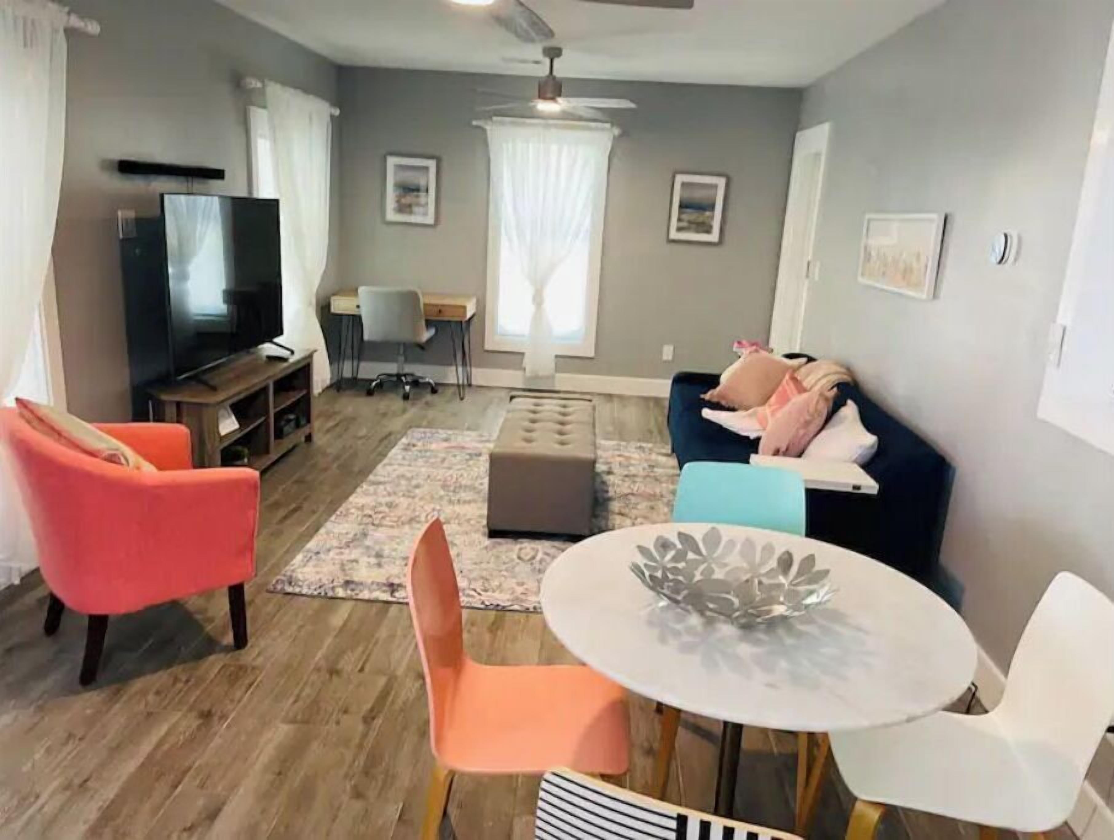 Un salon comprenant un téléviseur, un bureau, une chaise, un canapé et une table à manger avec des chaises.