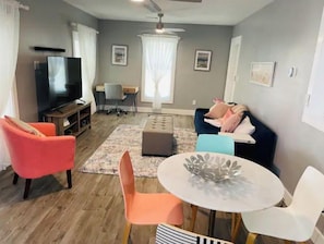 A living room with a TV, a desk, a chair, a sofa, and a dining table with chairs.