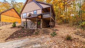 A two-story cabin with a stone foundation and a wooden upper structure, featuring a balcony and a stone entrance. - Great Location, 3 min To Parkway! Private Hot Tub,Arcade, Fireplace,shuffleboard (Pigeon Forge)