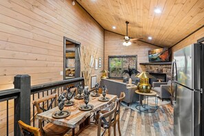 A cozy cabin interior with a dining area, a fireplace, and a kitchen. - Great Location, 3 min To Parkway! Private Hot Tub,Arcade, Fireplace,shuffleboard (Pigeon Forge)