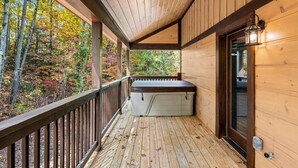 A wooden deck with a hot tub, a wooden railing, and a view of autumn foliage. - Great Location, 3 min To Parkway! Private Hot Tub,Arcade, Fireplace,shuffleboard (Pigeon Forge)
